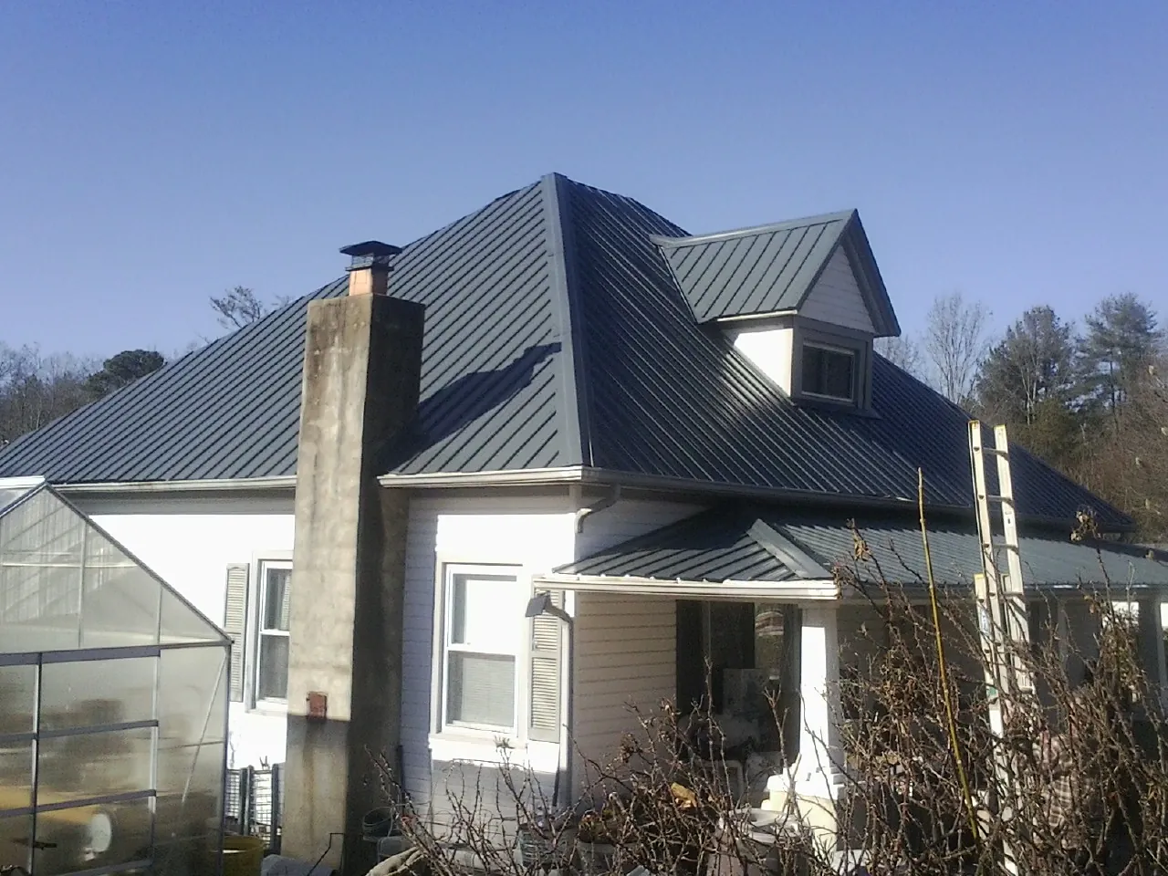 Dark blue standing seam metal roof on a white farmhouse with dormer — Slate & Tile Roof Repair by Roofing Brothers in Rutland