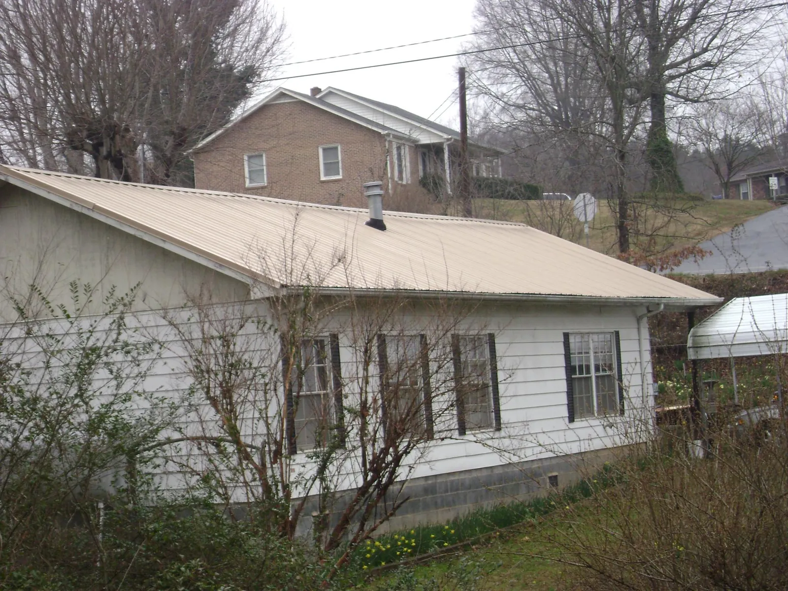 Tan metal roof on a white sided house set into a hillside — Commercial Roofing by Roofing Brothers in Rutland